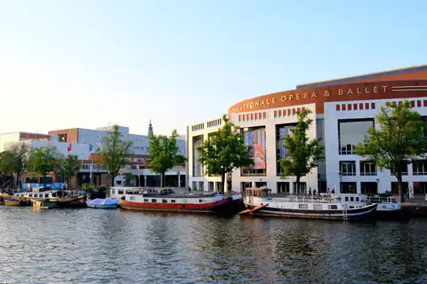 Edificio de la Stopera, sede del ayuntamiento y la Ópera Nacional, junto al río Amstel con barcos amarrados en Ámsterdam