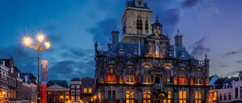 Fachada iluminada del ayuntamiento histórico de Delft, con su torre, en la plaza del mercado al anochecer