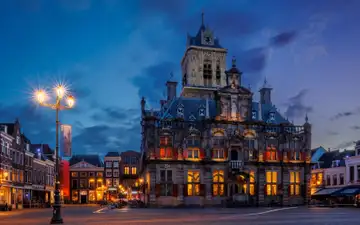Fachada iluminada del ayuntamiento histórico de Delft, con su torre, en la plaza del mercado al anochecer