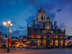 Fachada iluminada del ayuntamiento histórico de Delft, con su torre, en la plaza del mercado al anochecer