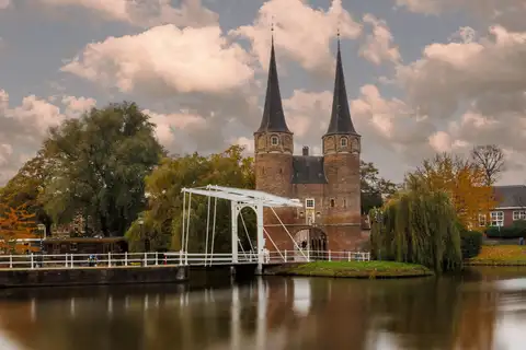 La puerta Oostpoort de Delft, con sus dos torres de aguja y un puente levadizo blanco reflejados en el agua en otoño