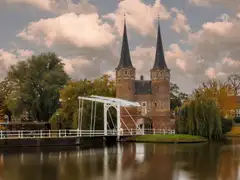 La puerta Oostpoort de Delft, con sus dos torres de aguja y un puente levadizo blanco reflejados en el agua en otoño