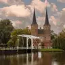 La puerta Oostpoort de Delft, con sus dos torres de aguja y un puente levadizo blanco reflejados en el agua en otoño