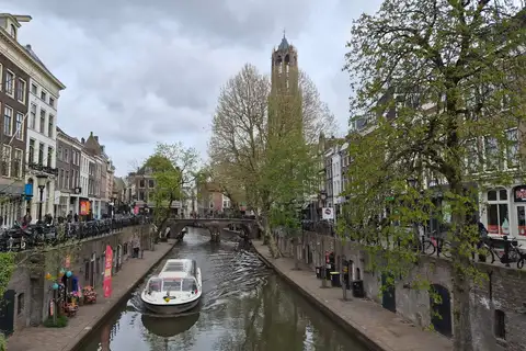 Canal Oudegracht de Utrecht con muelles a nivel del agua, un barco turístico y la torre Dom al fondo