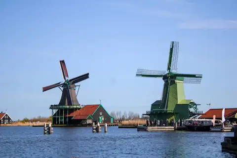 Dos molinos de madera verdes y casas de tejado rojo junto al río Zaan en Zaanse Schans, bajo cielo azul