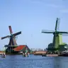 Dos molinos de madera verdes y casas de tejado rojo junto al río Zaan en Zaanse Schans, bajo cielo azul