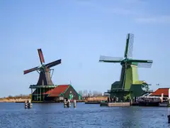 Dos molinos de madera verdes y casas de tejado rojo junto al río Zaan en Zaanse Schans, bajo cielo azul