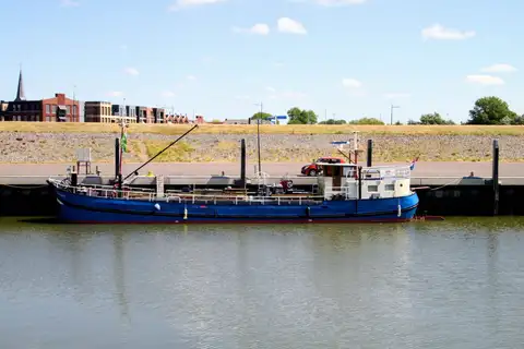 Antigua barcaza azul amarrada en el muelle del puerto de Harlingen, en Frisia, con edificios y una torre de iglesia al fondo