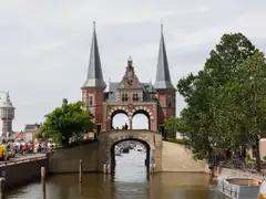 La Waterpoort de ladrillo rojo de Sneek, con dos torres de aguja, sobre el canal y con ciclistas en la orilla