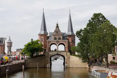 La Waterpoort de ladrillo rojo de Sneek, con dos torres de aguja, sobre el canal y con ciclistas en la orilla