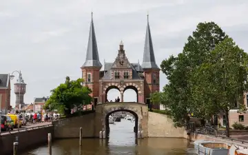 La Waterpoort de ladrillo rojo de Sneek, con dos torres de aguja, sobre el canal y con ciclistas en la orilla