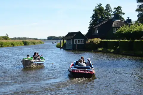 Dos barcas a motor en aguas abiertas con juncales y una casa de tejado de junco, en la zona de Giethoorn