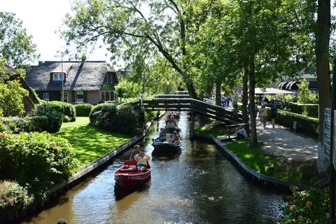 Casas con tejado de junco, puente de madera y barcas por un canal arbolado de Giethoorn en un día soleado