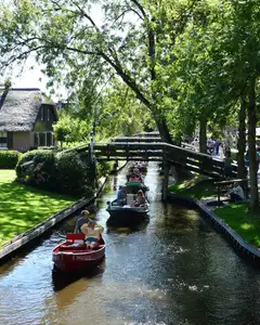 Casas con tejado de junco, puente de madera y barcas por un canal arbolado de Giethoorn en un día soleado