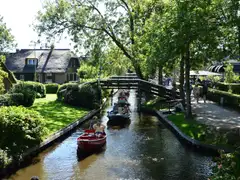 Casas con tejado de junco, puente de madera y barcas por un canal arbolado de Giethoorn en un día soleado