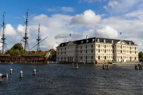 Réplica del velero de la VOC Amsterdam amarrada junto al edificio del Museo Marítimo Het Scheepvaartmuseum, bajo cielo azul