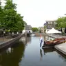 Bandera tricolor de los Países Bajos junto a un canal urbano con una barca de madera amarrada y edificios de ladrillo