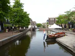 Bandera tricolor de los Países Bajos junto a un canal urbano con una barca de madera amarrada y edificios de ladrillo