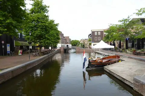 Bandera tricolor de los Países Bajos junto a un canal urbano con una barca de madera amarrada y edificios de ladrillo