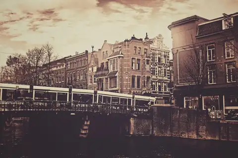 Tranvía cruzando un puente sobre un canal de Ámsterdam junto a casas históricas, en tonos sepia