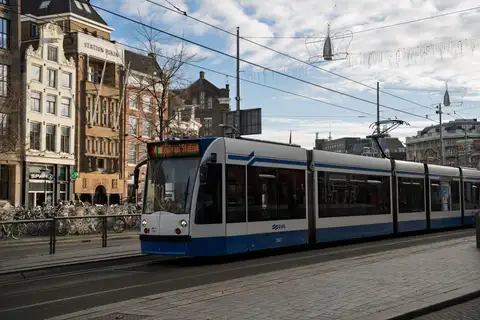 Tranvía azul y blanco de GVB frente a la estación Centraal de Ámsterdam con bicicletas aparcadas y fachadas históricas