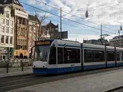 Tranvía azul y blanco de GVB frente a la estación Centraal de Ámsterdam con bicicletas aparcadas y fachadas históricas