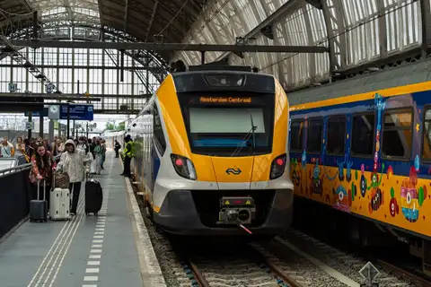 Tren de NS llegando al andén de la estación Amsterdam Centraal con viajeros con maletas bajo la marquesina