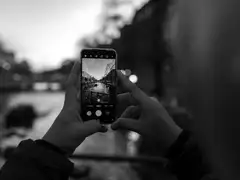 Manos sosteniendo un teléfono móvil cuya pantalla muestra un canal de Ámsterdam al anochecer, en blanco y negro