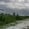 Hilera de molinos de Kinderdijk a lo largo de un canal con juncos y nenúfares en primer plano, bajo un cielo nublado