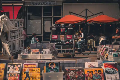 Puestos de mercadillo callejero con discos de vinilo, láminas y camisetas junto a una terraza en el barrio del Jordaan de Ámsterdam