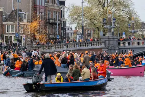 Multitud vestida de naranja en barcas junto a un puente con balaustrada sobre un canal de Ámsterdam durante el Día del Rey