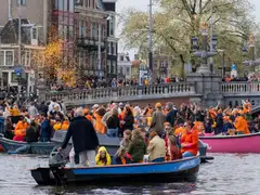 Multitud vestida de naranja en barcas junto a un puente con balaustrada sobre un canal de Ámsterdam durante el Día del Rey