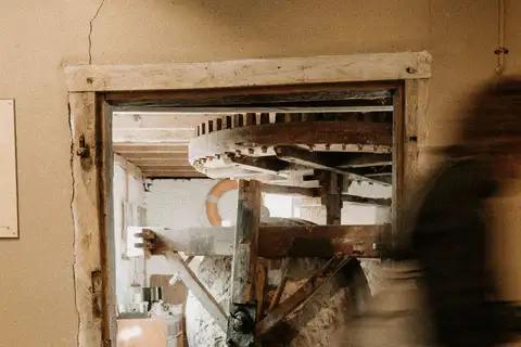 Interior de un molino histórico visto por una puerta de madera, con una gran rueda dentada de madera, vigas y ejes