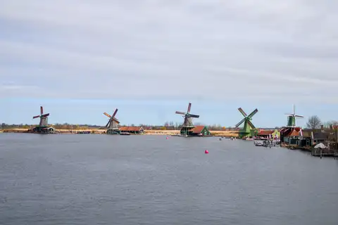 Hilera de molinos de madera a orillas del río Zaan en Zaanse Schans, con casas verdes y rojas y un cielo nublado