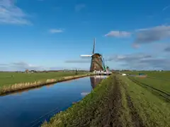 Molino de viento tradicional junto a un canal recto del pólder de Aarlanderveen, con prados verdes y un cielo azul con nubes