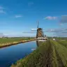 Molino de viento tradicional junto a un canal recto del pólder de Aarlanderveen, con prados verdes y un cielo azul con nubes