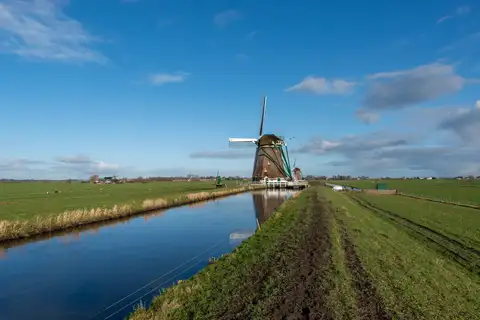 Molino de viento tradicional junto a un canal recto del pólder de Aarlanderveen, con prados verdes y un cielo azul con nubes