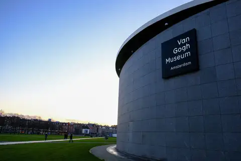 Fachada curva de granito del Museo Van Gogh con su rótulo, junto al parque de la Museumplein al atardecer