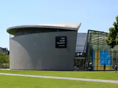 Fachada curva de granito y la entrada acristalada del Museo Van Gogh, con visitantes en el césped de la Museumplein