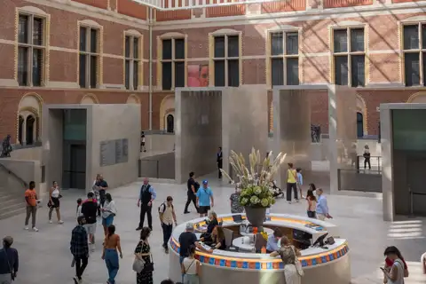 Visitantes en el atrio del Rijksmuseum alrededor del mostrador de información circular con un gran ramo de flores, bajo muros de ladrillo