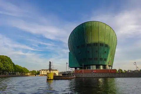 Edificio verde en forma de proa del museo NEMO a orillas del agua en Ámsterdam, con cielo azul y árboles al fondo