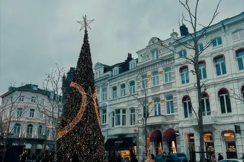 Gran árbol de Navidad cubierto de luces cálidas frente a elegantes edificios blancos del centro de Maastricht