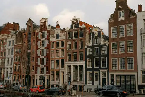 Fila de casas estrechas de ladrillo con frontones decorados y coches aparcados en la orilla de un canal de Ámsterdam