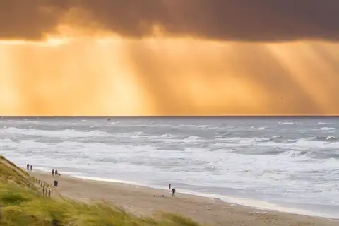 Playa de Zandvoort al atardecer con olas, rayos de luz entre las nubes y paseantes en la orilla