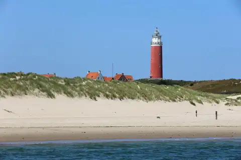 Dunas y playa de arena de Texel con el faro rojo de De Cocksdorp al fondo bajo un cielo azul
