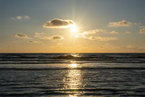 Puesta de sol dorada sobre el mar del Norte, con olas suaves y el reflejo del sol en la orilla