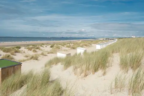 Ancha playa de arena con dunas cubiertas de hierba, casetas blancas de madera y el mar del Norte