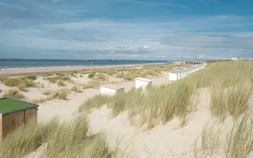 Ancha playa de arena con dunas cubiertas de hierba, casetas blancas de madera y el mar del Norte