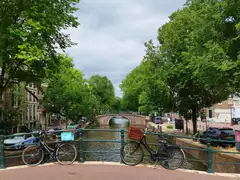Bicicletas aparcadas en un puente sobre un canal de Ámsterdam flanqueado de árboles y casas de ladrillo