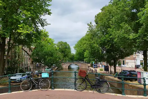 Bicicletas aparcadas en un puente sobre un canal de Ámsterdam flanqueado de árboles y casas de ladrillo